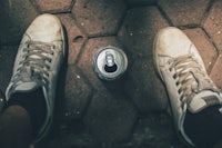 The image is taken from above. A can (of beer, perhaps?) sits between the legs of the phototaker, who is wearing grubby looking athletic shoes.